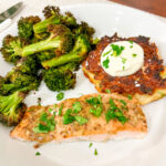 Baked honey mustard salmon on a white plate with roasted broccoli and a mashed potato cake.