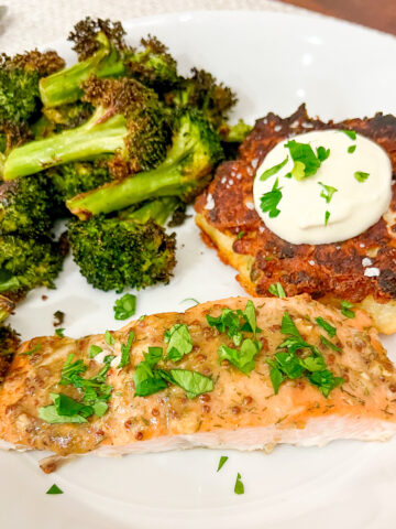 Baked honey mustard salmon on a white plate with roasted broccoli and a mashed potato cake.