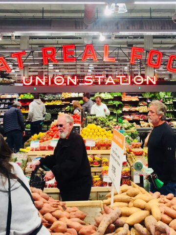 People grocery shopping in the Whole Foods produce section.