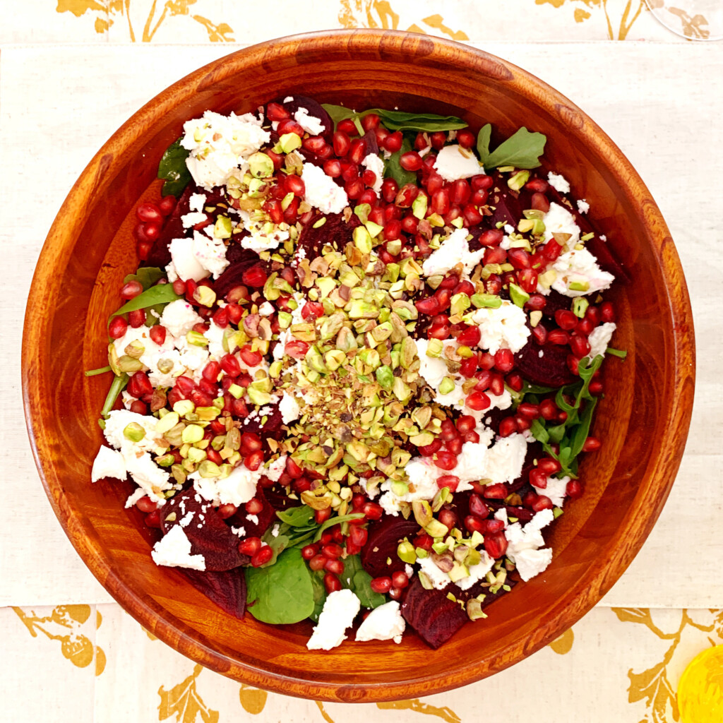 Beet and spinach salad in a wood bowl on a gold and white tablecloth