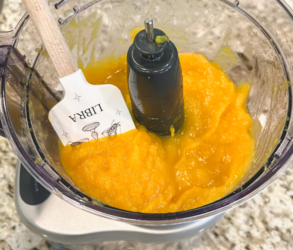 Pumpkin puree with a white spatula in a food processor on a counter top.