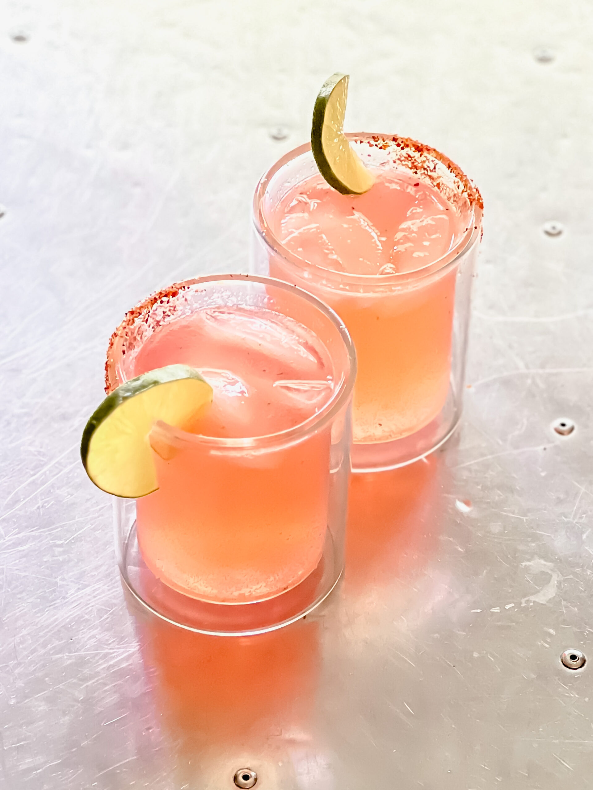 Blood orange margaritas with lime wedges on a silver table