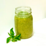 A mason jar filled with honey basil salad dressing on a white background with a basil leaf in the foreground