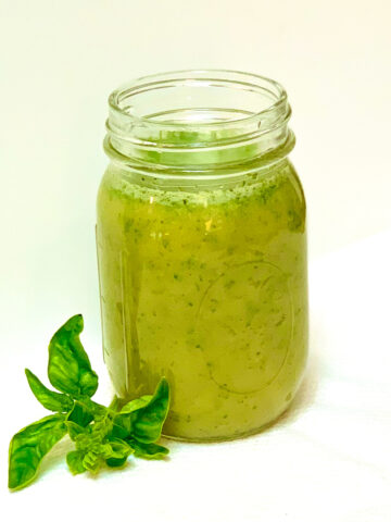 A mason jar filled with honey basil salad dressing on a white background with a basil leaf in the foreground