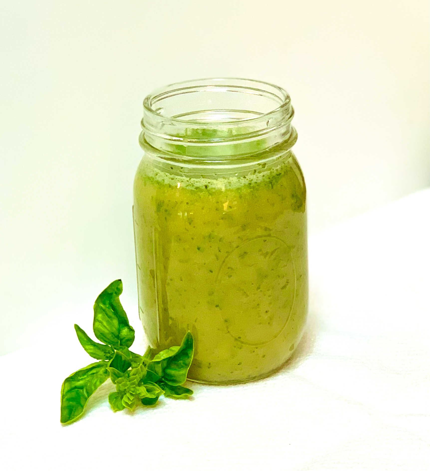 A mason jar filled with honey basil salad dressing on a white background with a basil leaf.