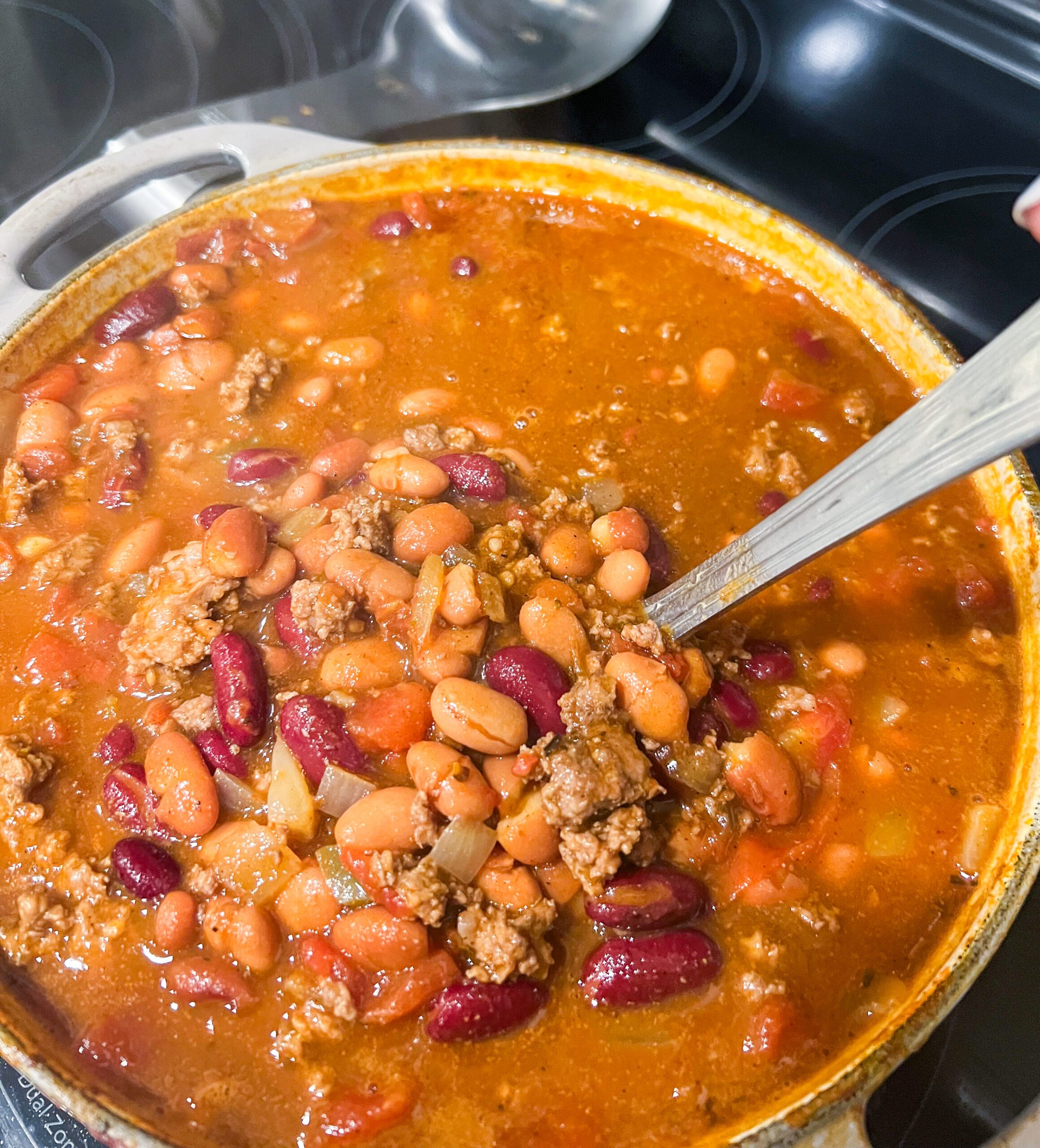 Close up of beef chili in a Dutch oven on a stovetop with a ladle.