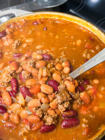 Close up of beef chili in a Dutch oven on a stovetop with a ladle.