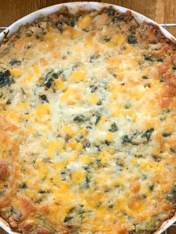 Spinach artichoke dip in a white baking dish on a silver cooling rack on a table.