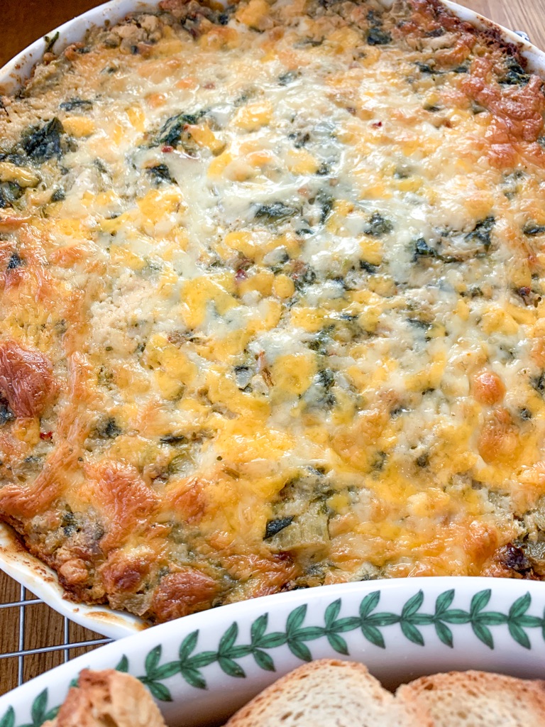 Spinach artichoke dip in a white baking dish on a silver cooling rack on a table.