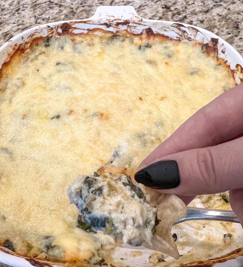 A hand scooping a chip with spinach artichoke dip in it.