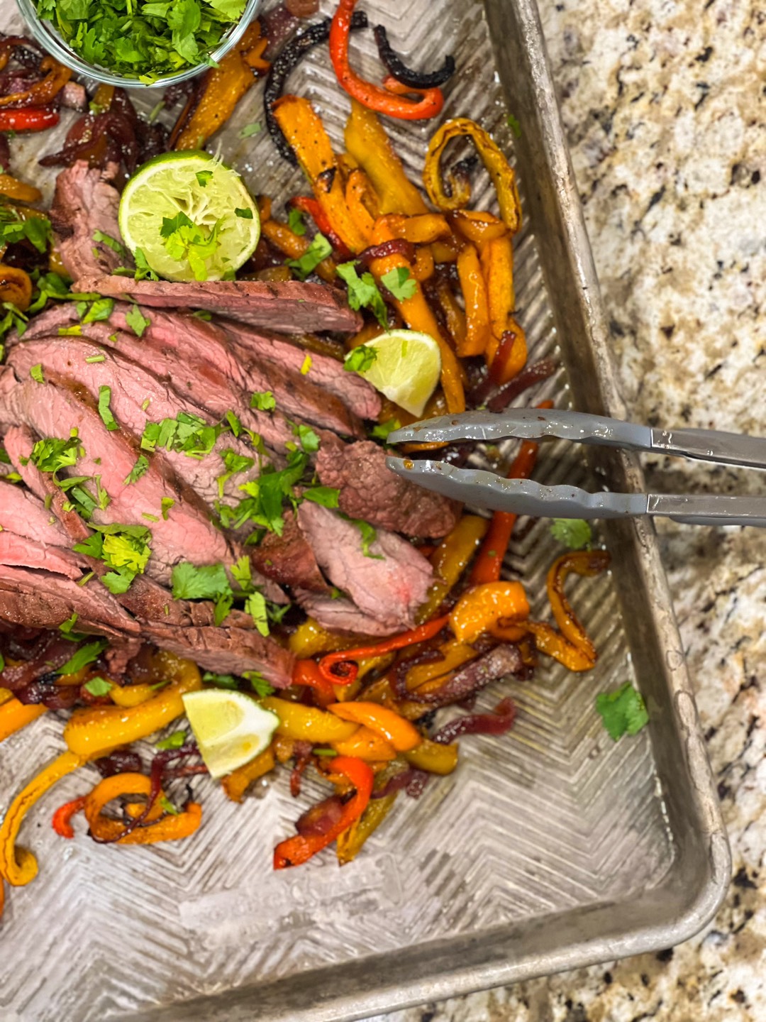 Flank steak fajitas on a sheet pan on a countertop.