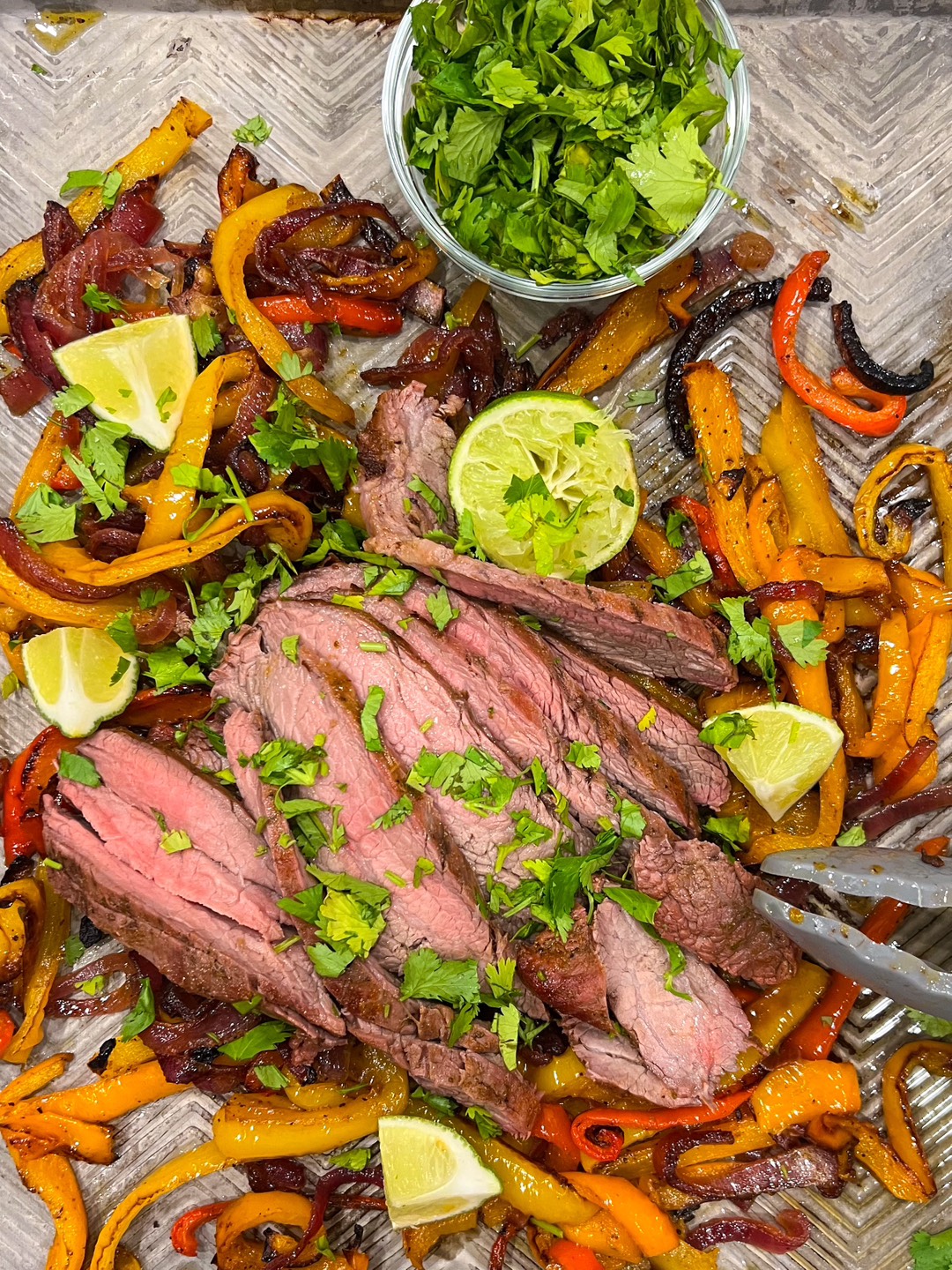 Flank steak fajitas on a sheet pan on a countertop.