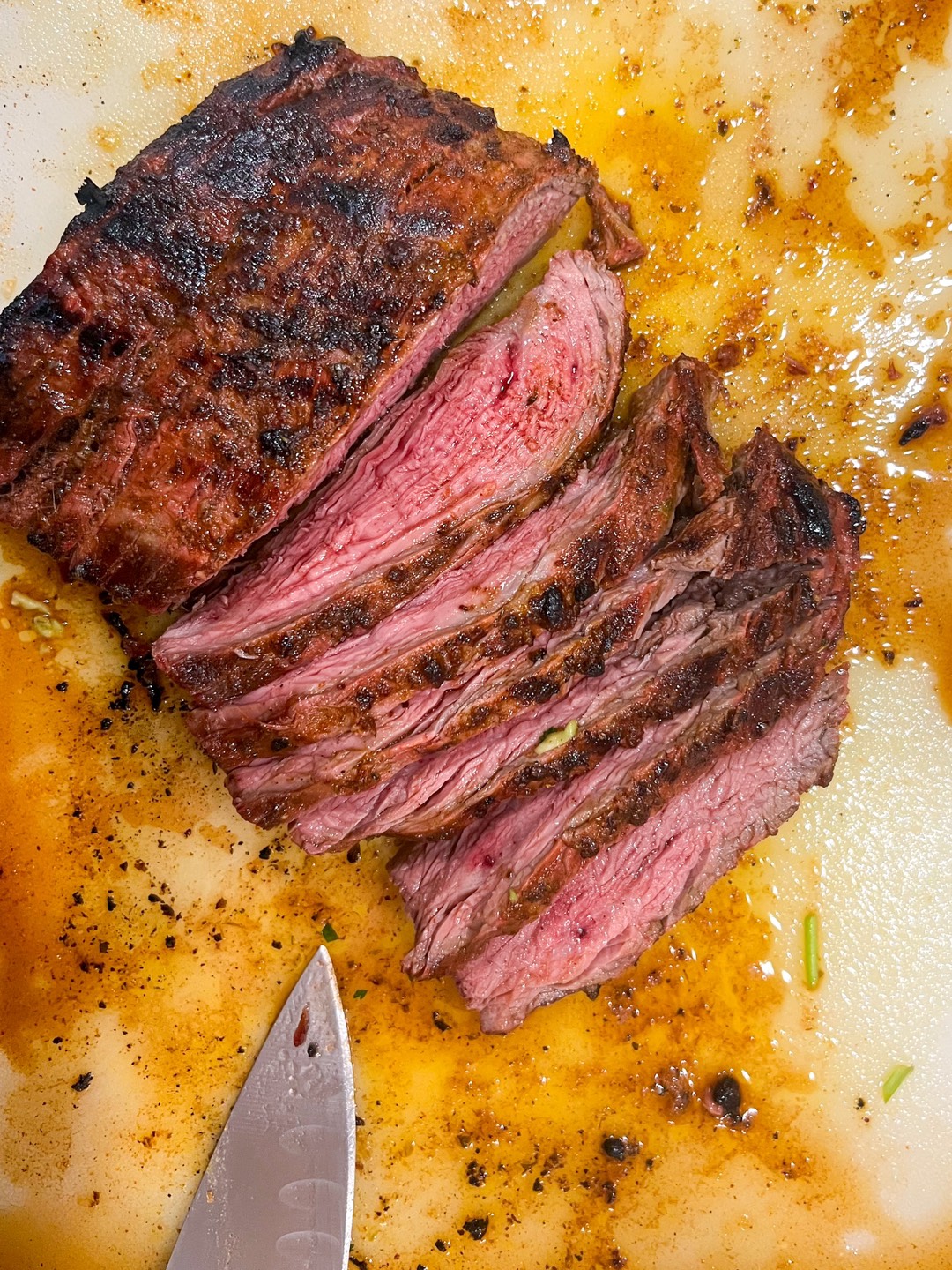 Grilled and sliced flank steak on a cutting board with a knife.